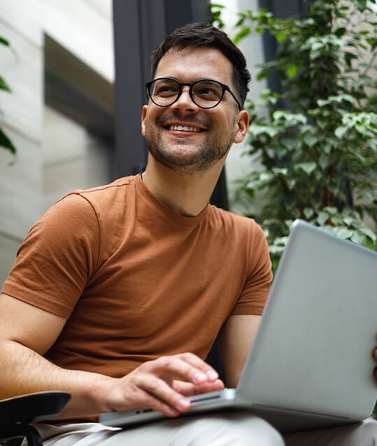 A smiling man who is working on the laptop